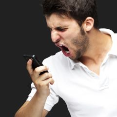 portrait of angry young man shouting using mobile over black bac